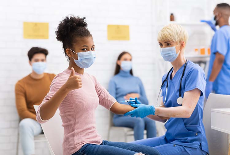 Young woman giving thumbs-up sign as she gets her vaccination