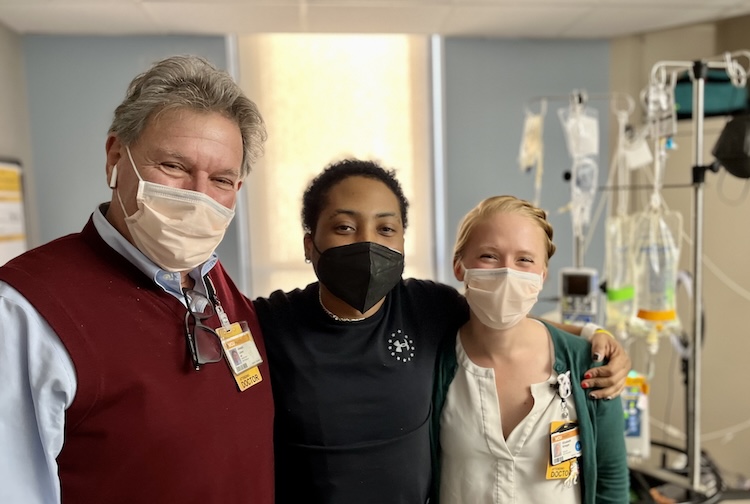 Two vcu health team members stand with a patient who participated in the gene therapy clinical trial for sickle cell disease. They are in a hospital room and are wearing facemasks.