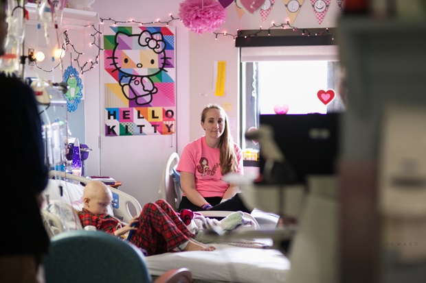 Katie Whatley sits in a hospital bed while her mother, Amanda Whatley, sits in a chair alongside the bed.