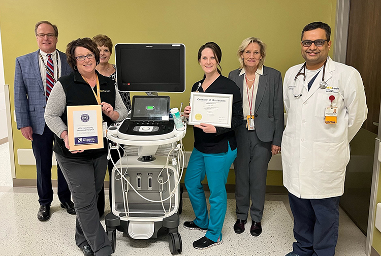 A group of health care workers stand with certificates and an echocardiography machine.