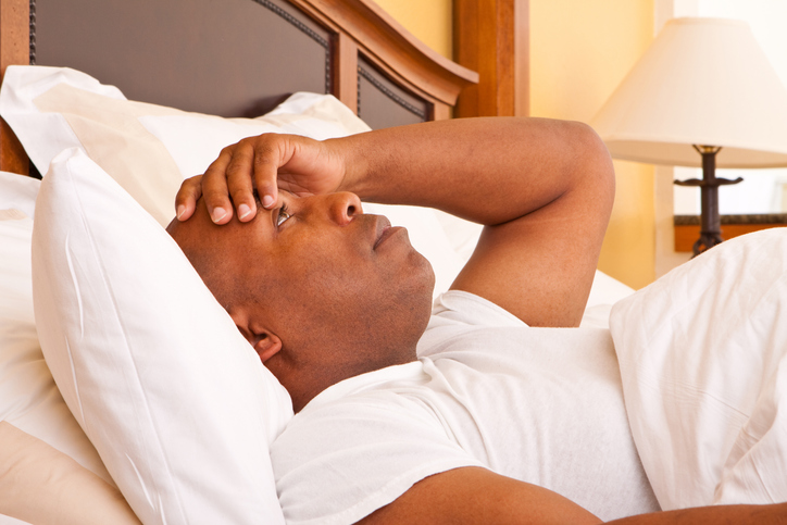 African-American male laying in bed with hand on forehead and eyes open