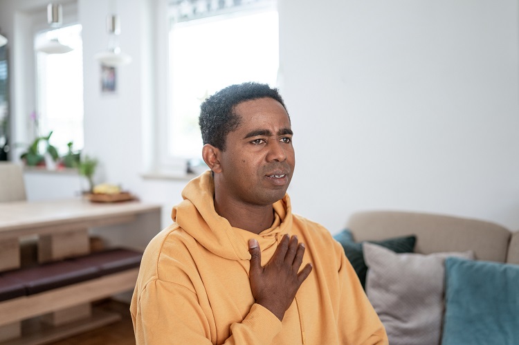 Male wearing an orange hoodie holding his hand on his chest with a concerned look