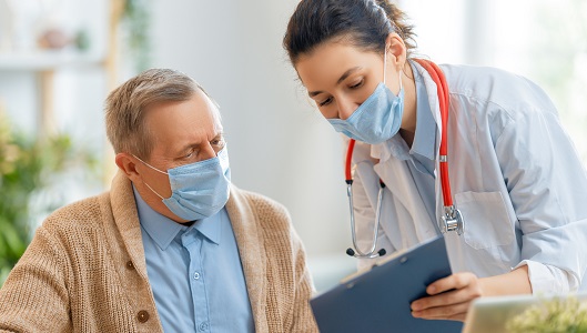 Older white man wearing a mask and woman health care provider wearing a mask looking at clipboard 