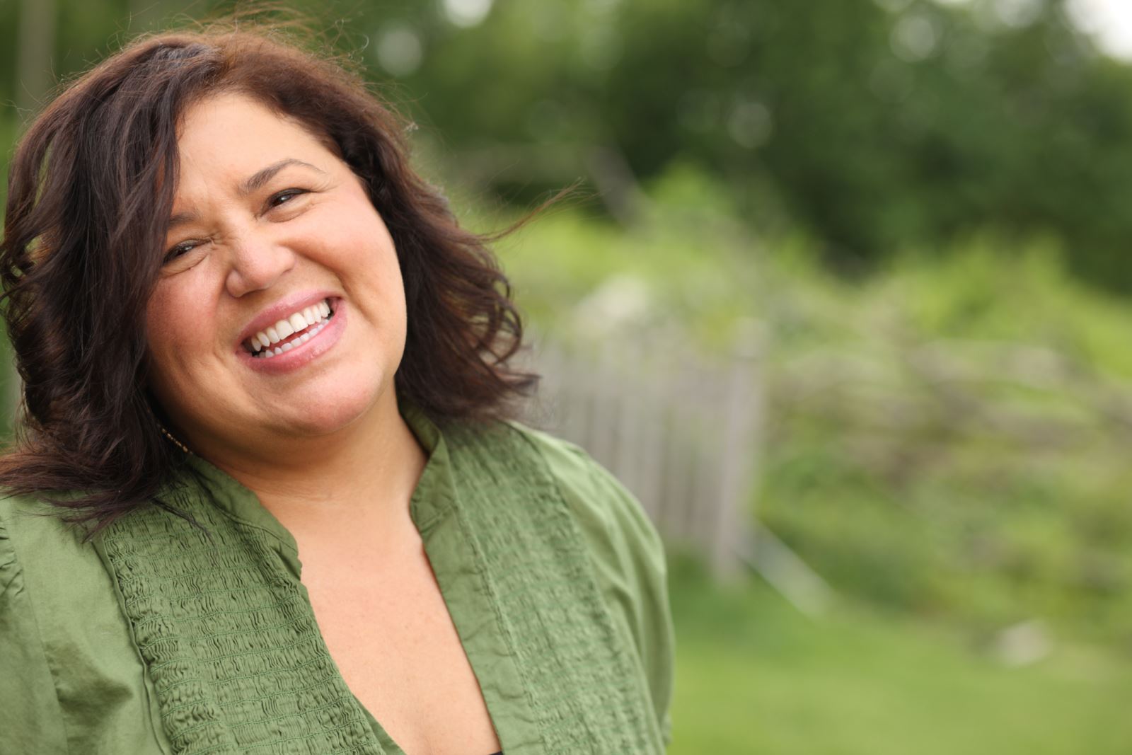 Hispanic woman wearing a green shirt smiling outside. 