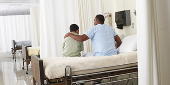 Adult patient sitting on a hospital bed with his arm around the child sitting next to him.