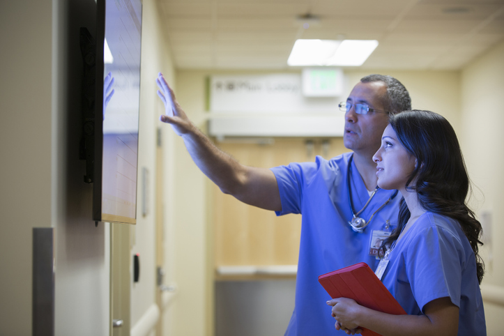 Two doctors looking at at a large monitor in a hospital hallway