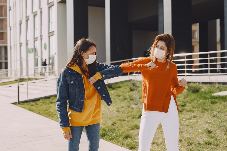 Two women wearing masks and bumping elbows
