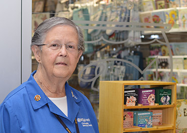 A lady wearing a blue jacket stands in front of a hospital gift shop.