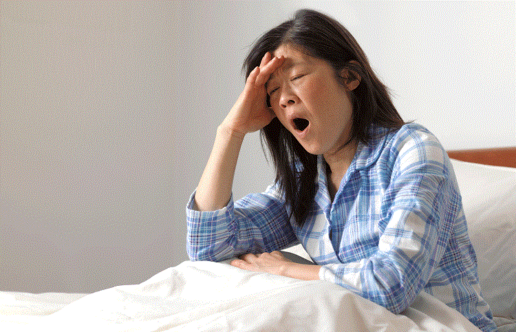 Woman sitting in bed with hand on her forehead and yawning