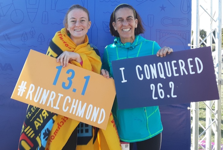 Two women standing in rain jackets with signs after a race.