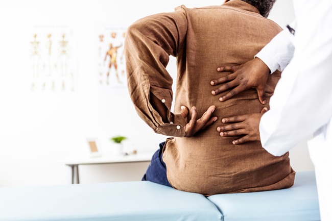 A patient points to his back while a doctor exams him.