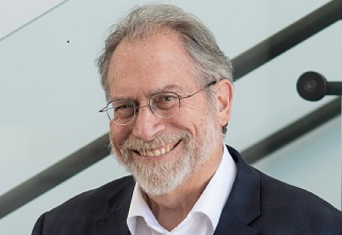 man smiling for a headshot. he is in a suit and wears glasses.
