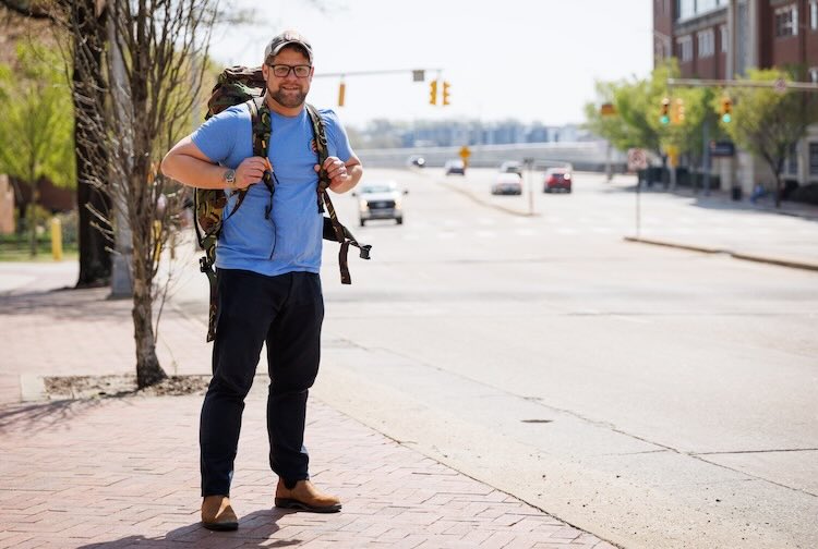 Keith stands with a hiking backpack along a busy street on VCU Health’s downtown Richmond campus