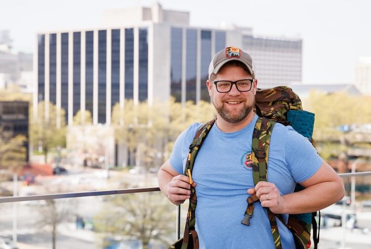 Keith smiles while holding the straps on his hiking backpack, which is filled with equipment to provide help if there’s an emergency on a trail