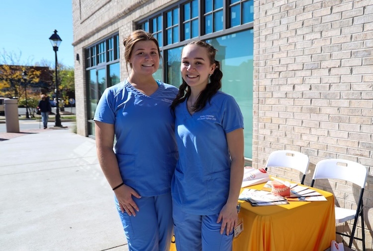 Two VCU students stand outside of the Health Hub at a table.