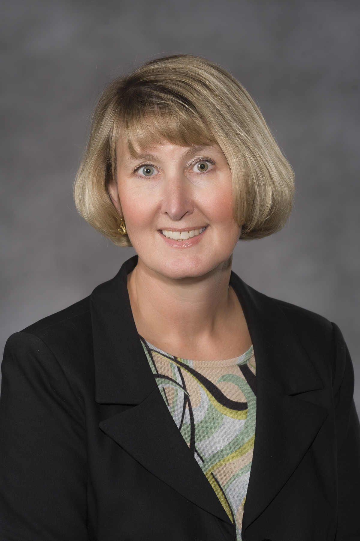 Dr. Goode is wearing a black suit jacket and green patterned shirt.