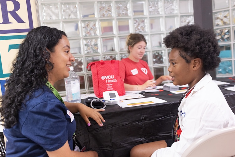 Boy in a lab coat speaks to Pauley Heart Center team member as part of Teach BP