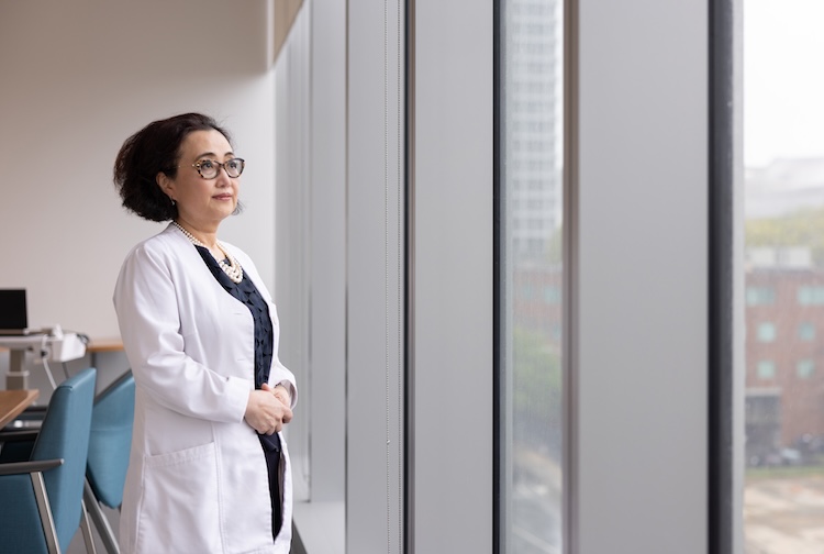 Woman in white medical coat stares out a large window