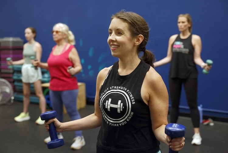Dr. Kimbrough stands in the front of a class holding weights.