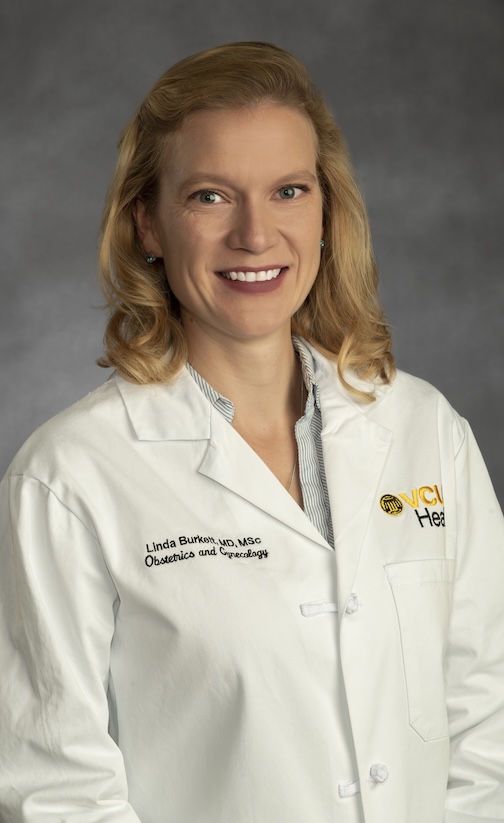 Dr. Burkett is wearing a blue collared shirt and her white medical jacket.