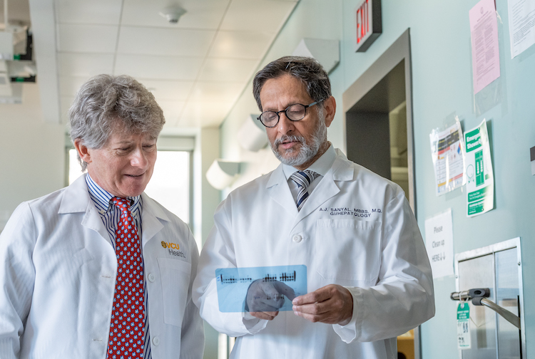 Two men standing with white coats looking at data in a hallway. 