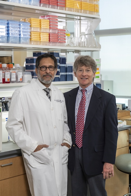 Dr. Sanyal stands in a lab in a white medical coat with Dr. Stravitz, who is wearing a suit.