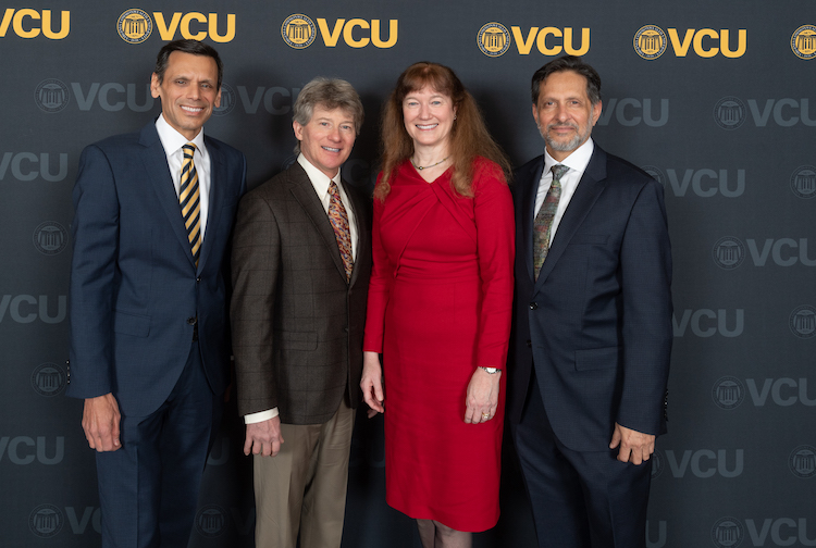Four people pose in front of a VCU backdrop