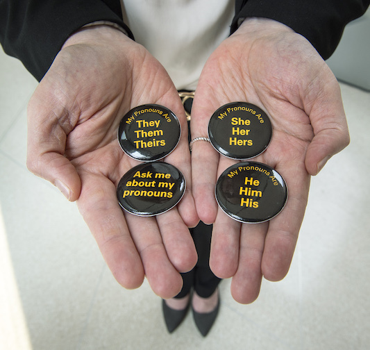 Four pins with a variety of pronouns on them lay flat on a person's hands.
