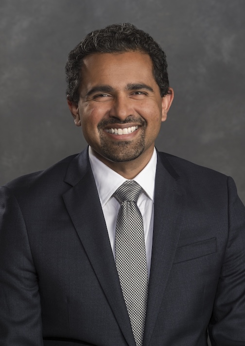 Dr. Pillai smiles while wearing a black suit