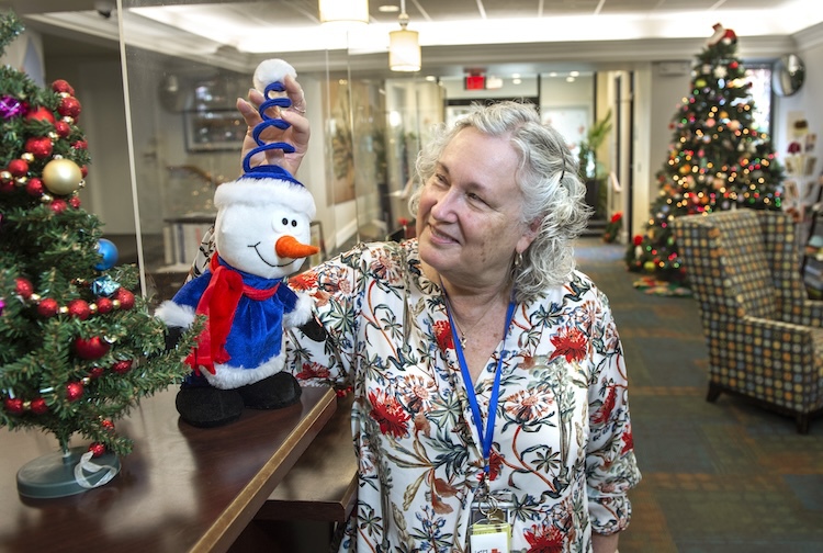 Woman smiles while standing next to a little snowman with a hat. She is playing with the hat.