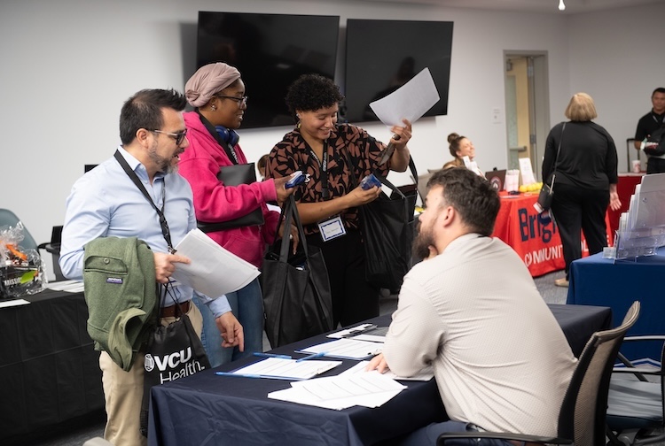 Patients and family members talking to a person sitting at a table at a job fair.
