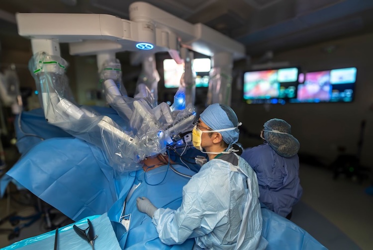 Surgeon sitting at operating table watching over robotic device to operate on patient