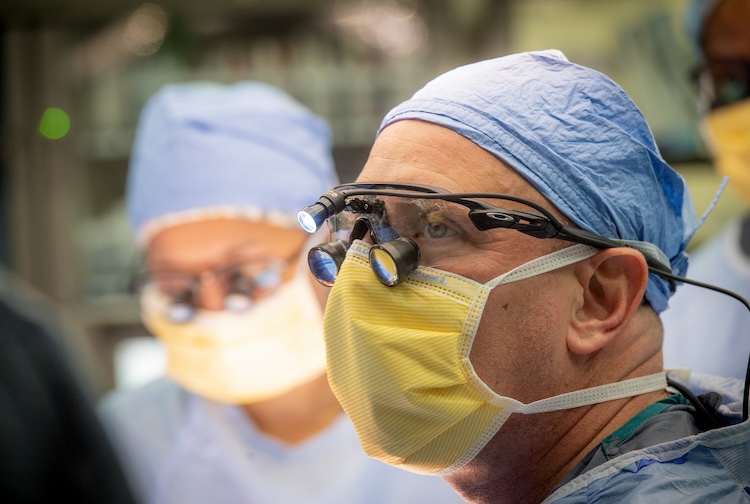 Bruno wears scrubs, a facemask and eyeglasses in a surgical suit