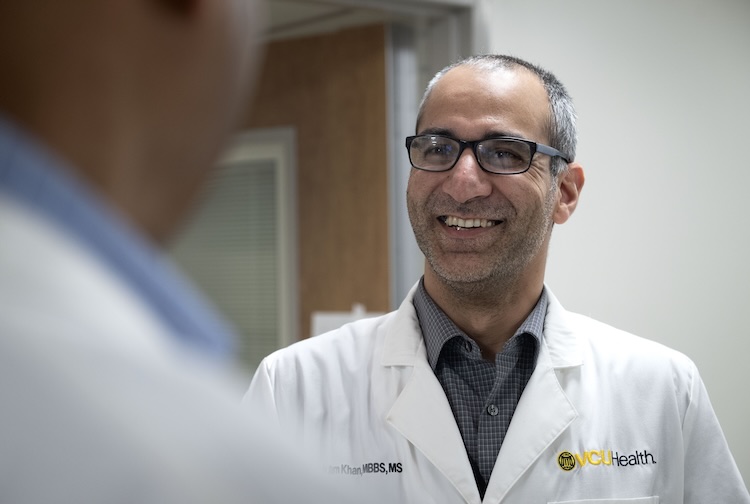 Dr. Khan smiles while wearing a medical white coat and talking to another VCU Health team member.