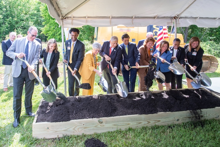 Group of people in suits and dresses dig into dirt with shovels