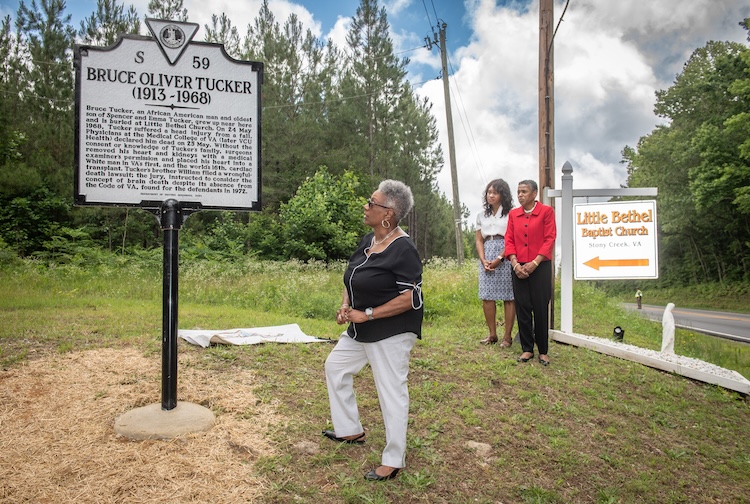 Woman stands and looks at historical highway marker with two women standing behind her.