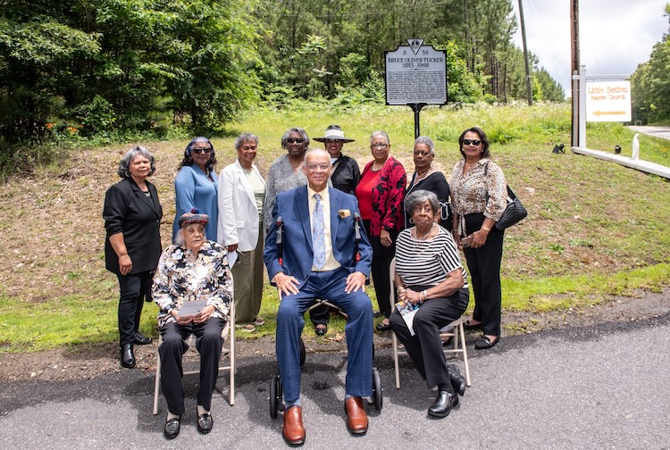 Members of Bruce Tucker’s family sit and stand in front of the new historical highway marker.