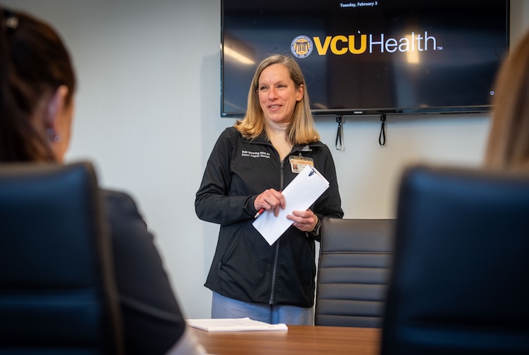 Beth stands at the front of a room speaking to team members.