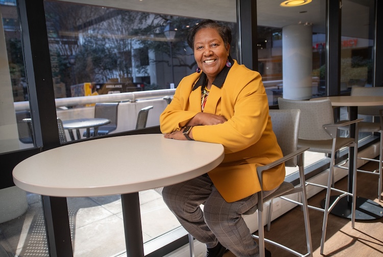 Janet sits at a table in a yellow suit jacket and black pants
