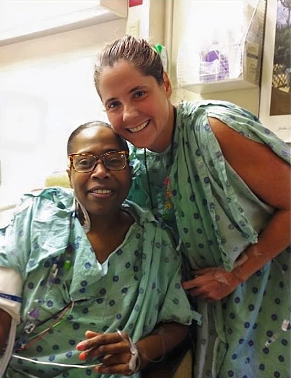 Tracey smiles with Djuna Paige, the woman who received her kidney donation. Both are in the hospital wearing hospital gowns.