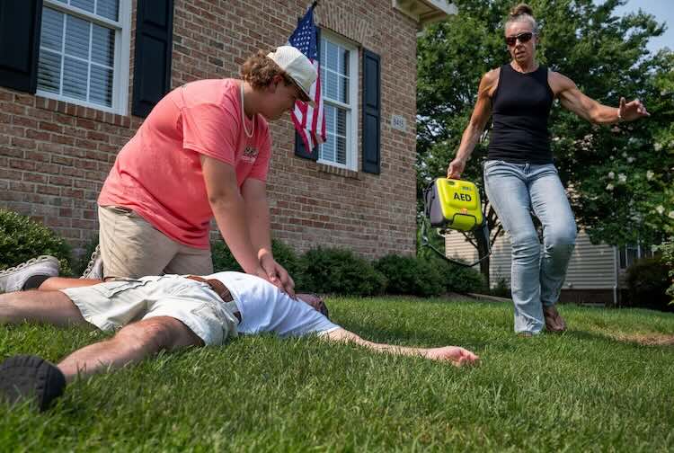Man giving chest compress to someone on the ground, while a women is carrying AED to them.