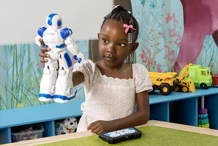 Little girl in light pink dress holding up a robot toy.