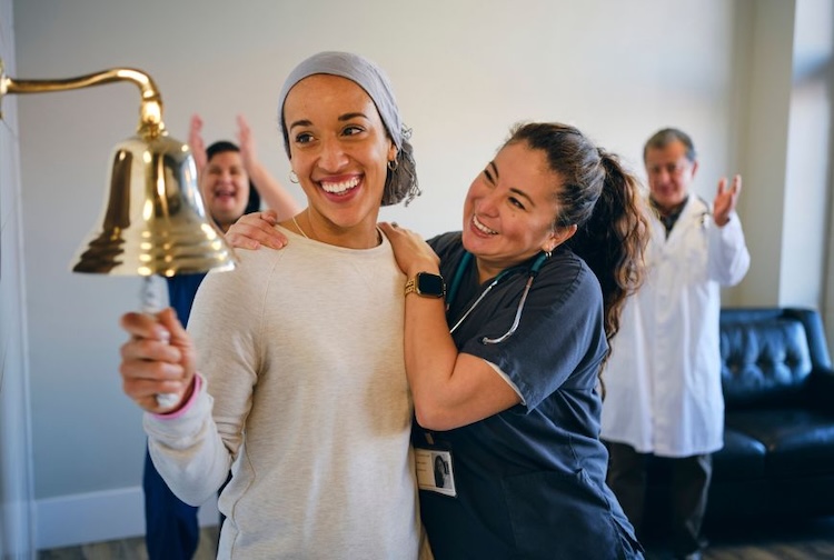 Patient smiles with her care team while ringing a bell after her last round of cancer treatment