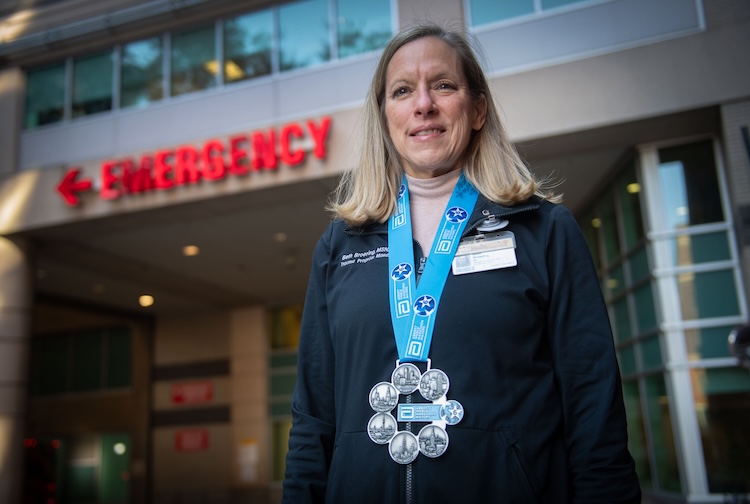 Beth stands near a hospital sign that says emergency while wearing a medal from a marathon.