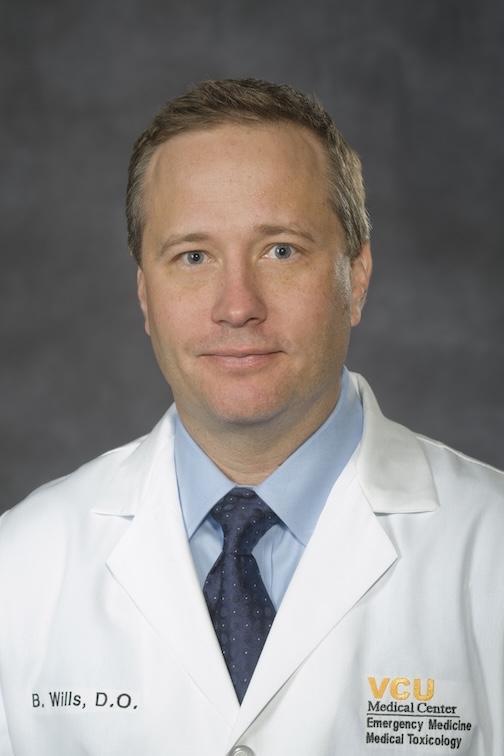 Dr. Wills is wearing a white medical coat and blue tie