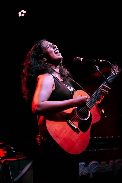 Sravani playing the guitar live while singing in a microphone.