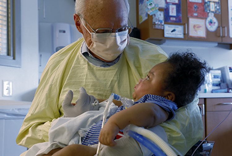 A older gentlemen holding a NICU baby in his arms.