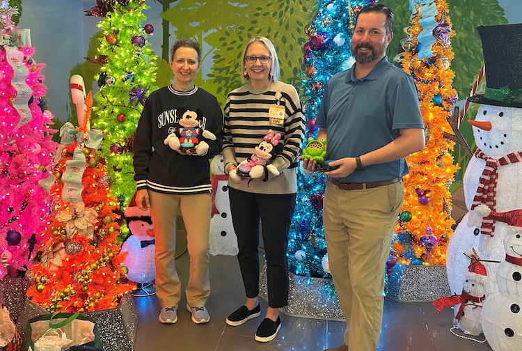 Three people holding toys in hands around christmas decorations