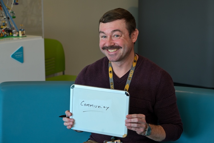 Joe holds a whiteboard with the word 'community' written on it