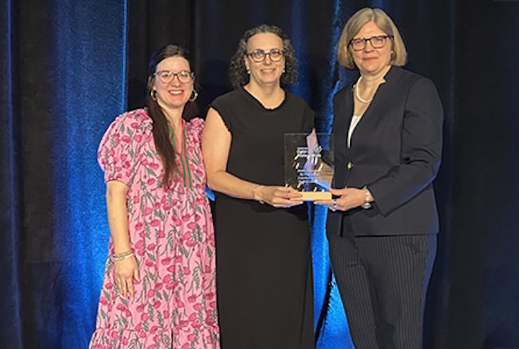 three women standing next to each other holding an award.